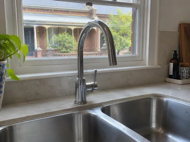 Chrome kitchen mixer tap over stainless steel sink beneath a window in a light-colored benchtop kitchen in Tempe